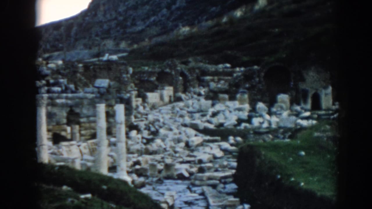 Stone ruins with columns, rubble, arched openings, and a rocky hillside.