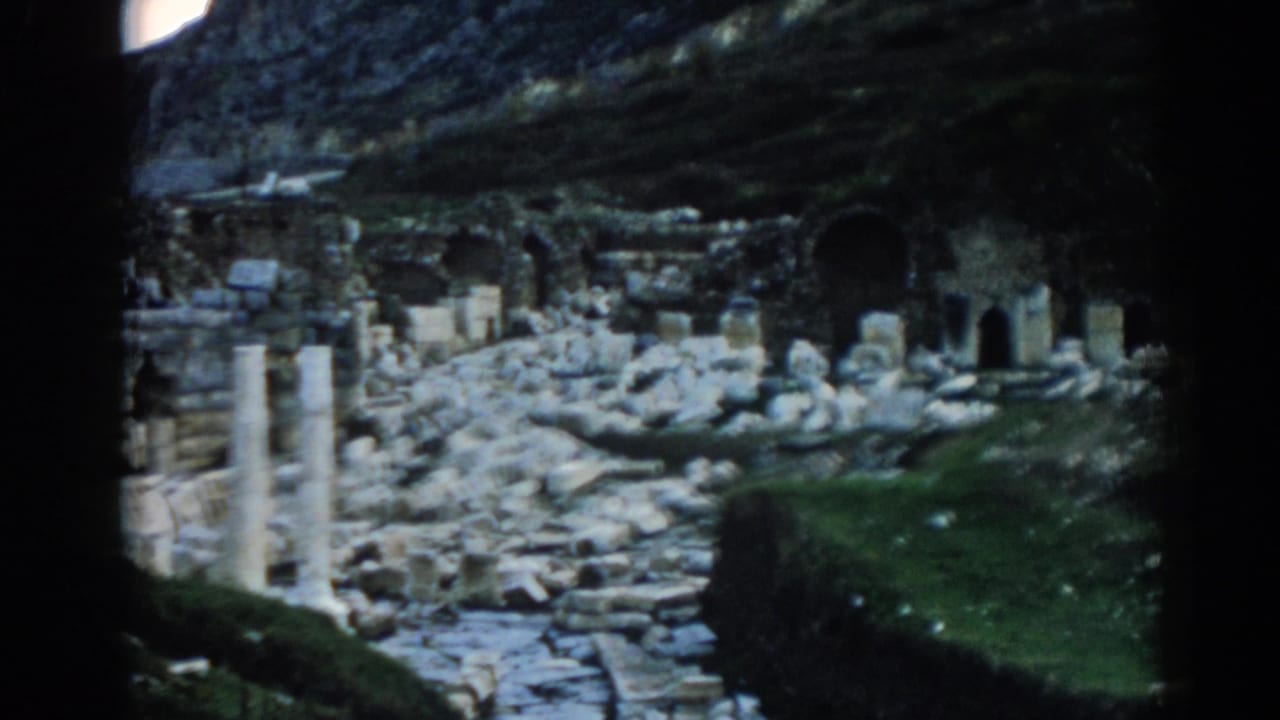 Vintage 8mm frame of Ephesus ruins showing broken stonework, two pale columns, arches, and shadowed frame edges.