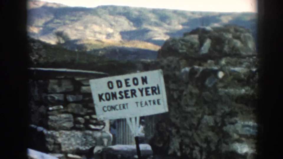 1962 Ephesus frame with an Odeon Konser Yeri Concert Theatre sign mounted near rough stonework and a sunlit hillside.