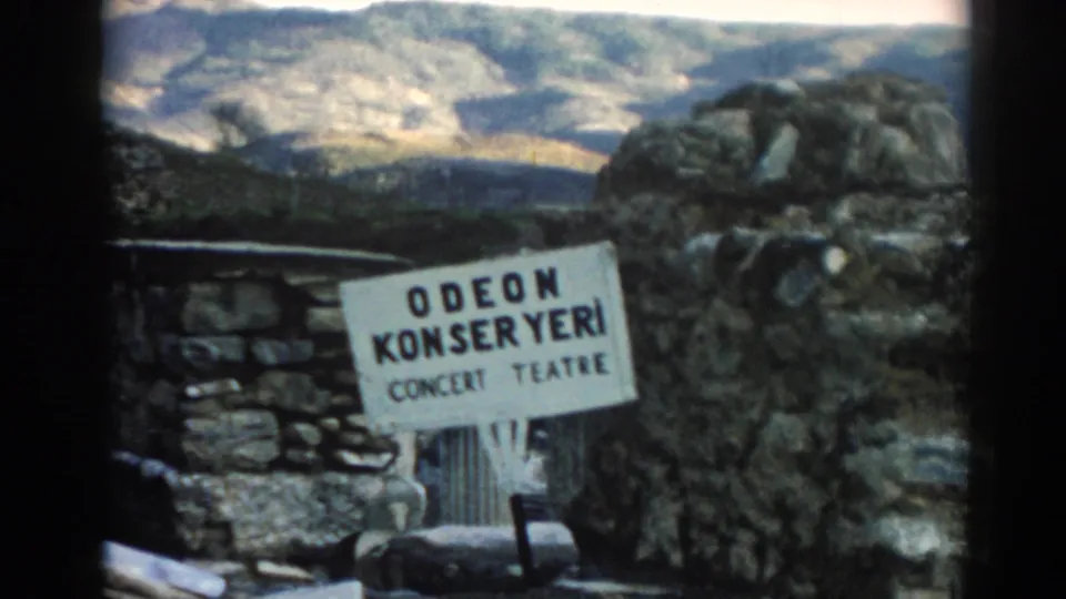 1962 Ephesus frame with the Odeon Konser Yeri sign in front of stonework and a sunlit rocky landscape.