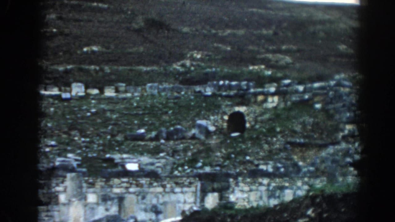 Grassy hillside ruins with low stone walls and a dark arched opening.