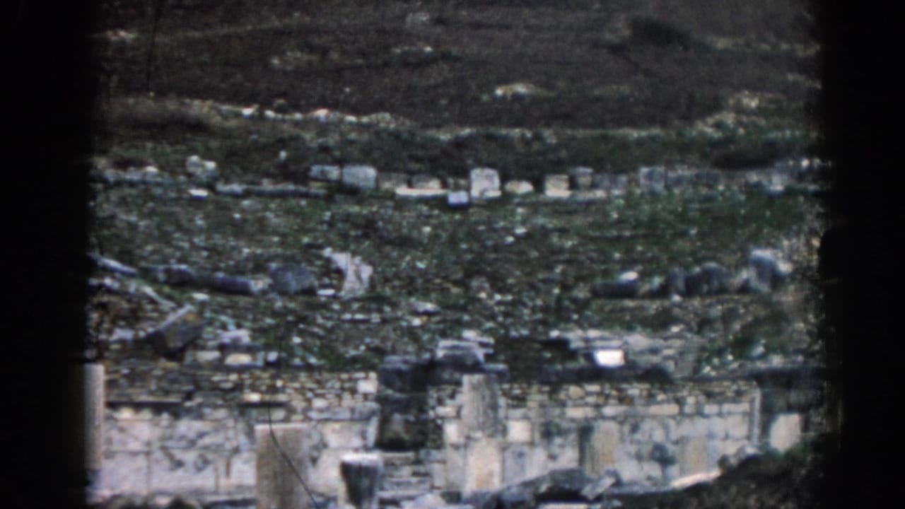 Distant hillside ruins with pale stone walls, scattered rocks, and dark terraced ground.