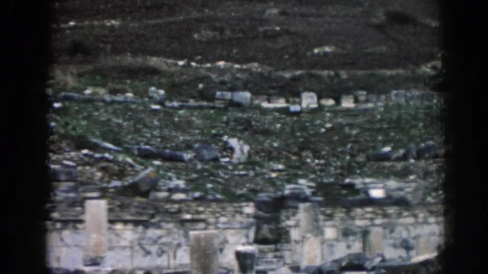 1962 Ephesus frame with weathered masonry, broken stones, and a muted hillside seen from a distant visitor viewpoint.