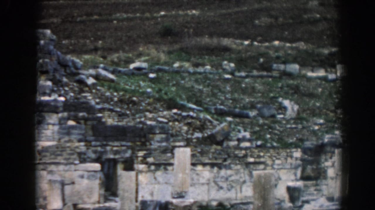 Grey stone ruins and scattered blocks on a cloudy hillside.