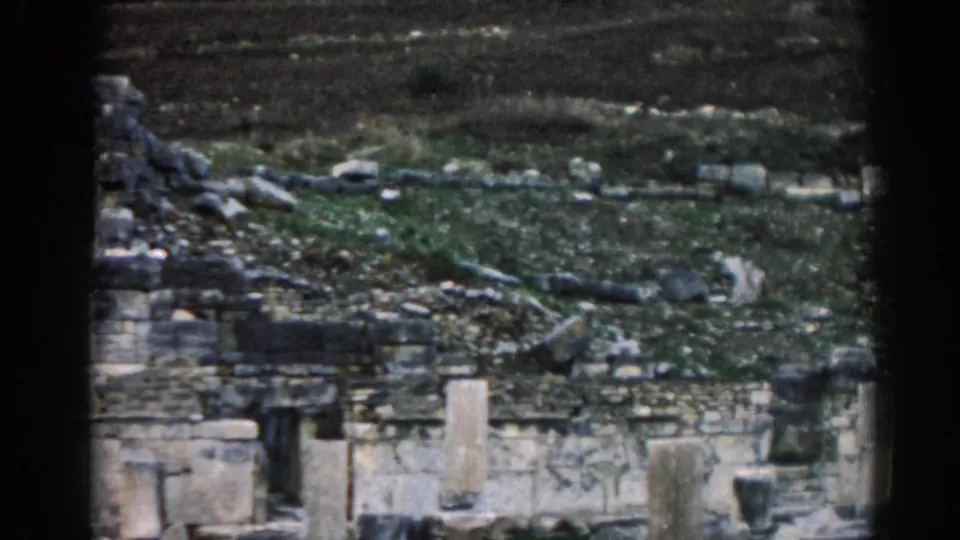 1962 8mm view of Ephesus, Turkey, showing weathered stone ruins, rubble, and muted green hillside ground.