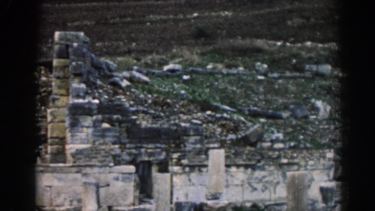 Ephesus ruin view with broken stone walls, upright masonry, scattered blocks, and dark hillside terrain in soft 8mm color.