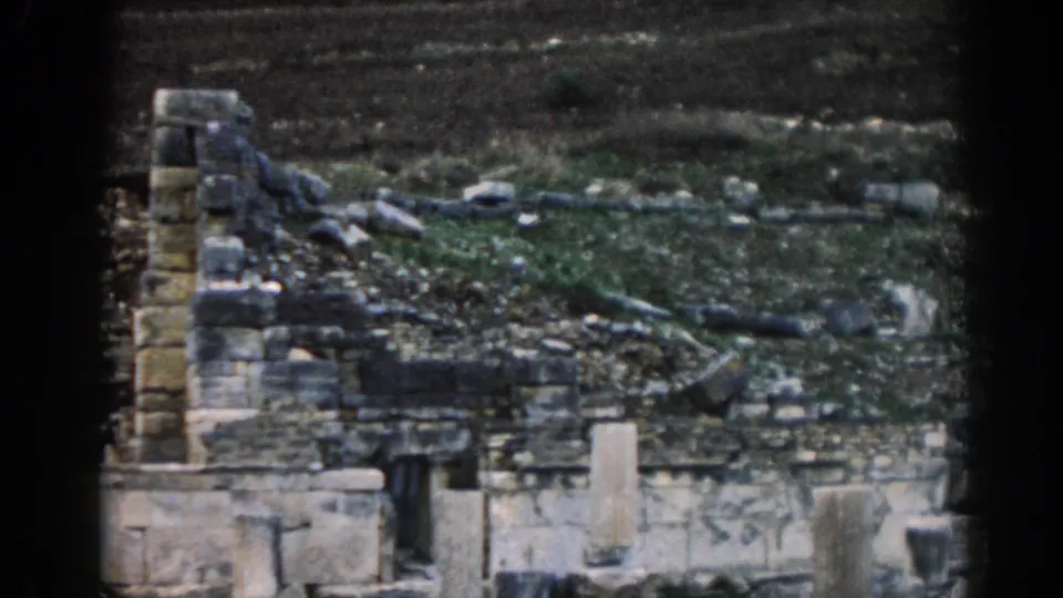 Ephesus ruin view with broken stone walls, upright masonry, scattered blocks, and dark hillside terrain in soft 8mm color.