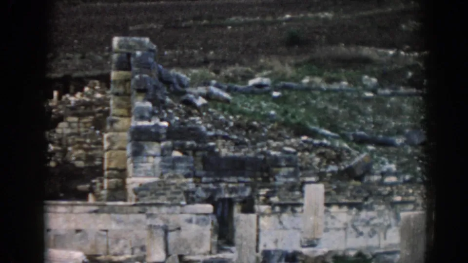 Mid-century Ephesus travel frame showing a vertical stone ruin section, low wall remains, rubble, and muted hillside vegetation.