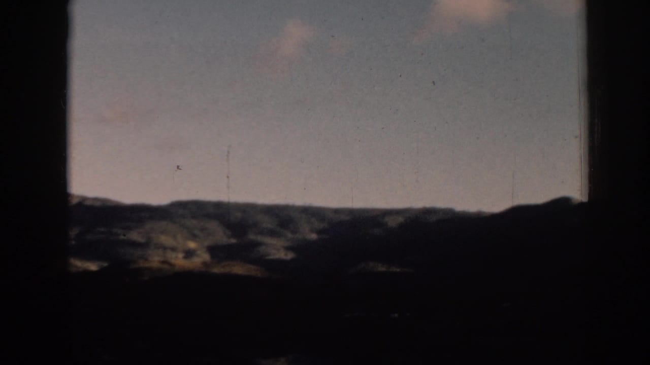 Distant hills and pale sky seen through a dark window or doorway.
