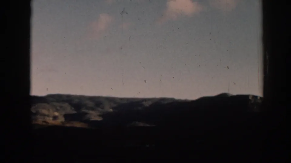 1962 home-movie frame from Ephesus showing a low mountain ridge and pale sky from a shaded viewpoint.