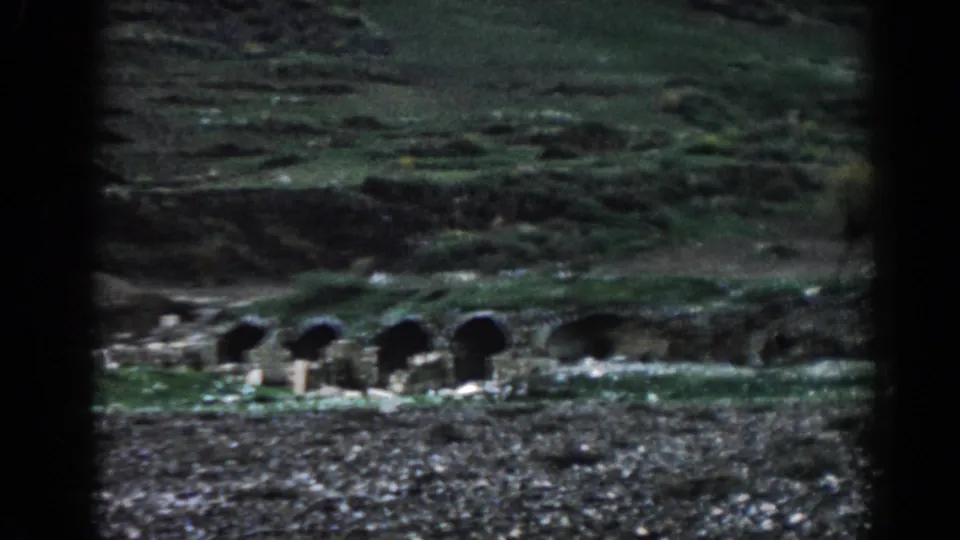 Ancient-looking stone arch openings beside water on a rocky green hillside in Ephesus, Turkey.