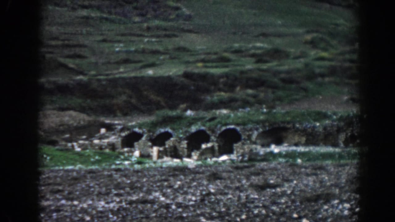 Distant stone arches set into a grassy hillside above rocky ground.