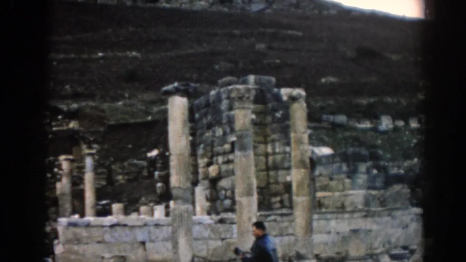 Closer 1962 Ephesus view with weathered columns, stone walls, and an adult visitor in a dark jacket.