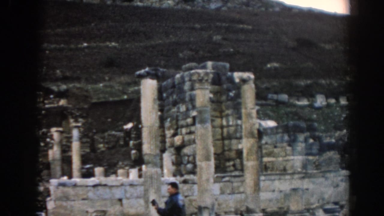 Stone columns and ruin walls at an archaeological site with a tourist partly visible near the lower edge.