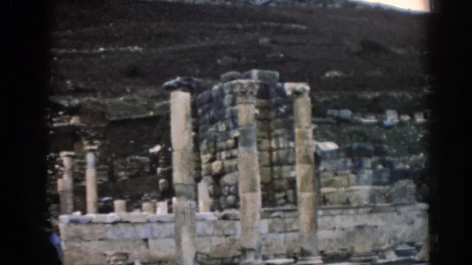 1962 Ephesus travel footage frame focused on standing columns, rough masonry, and low stone remains against a hillside.