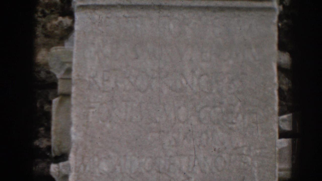 Weathered stone slab with faint carved inscriptions and dark film-edge framing.