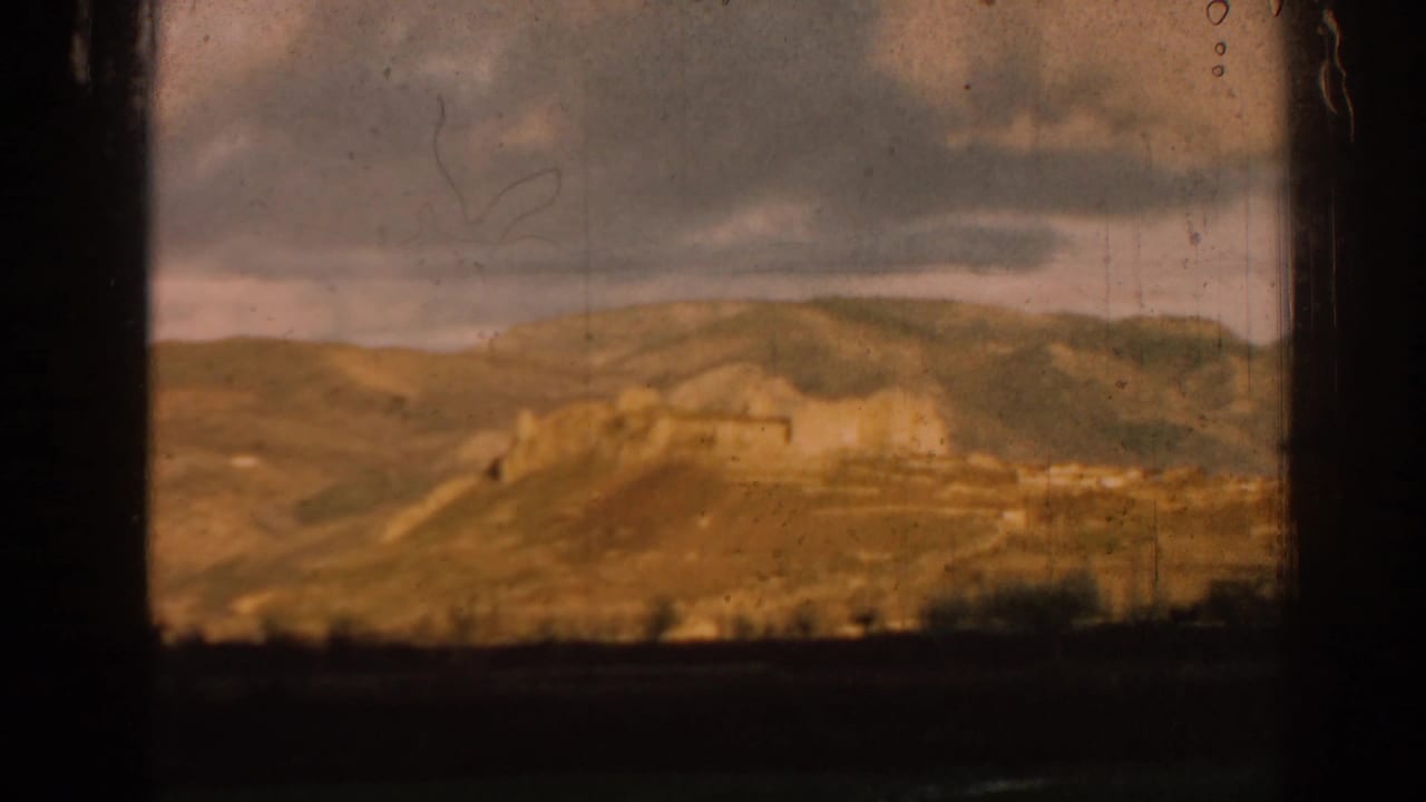 Rolling hills and distant ruin walls seen through dark film-frame borders.