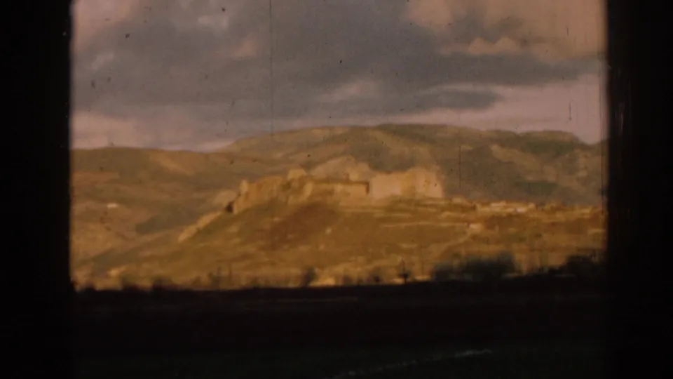 Final 1962 Ephesus landscape frame showing a distant castle-like ruin on hills, cloudy sky, and visible 8mm gate edges.