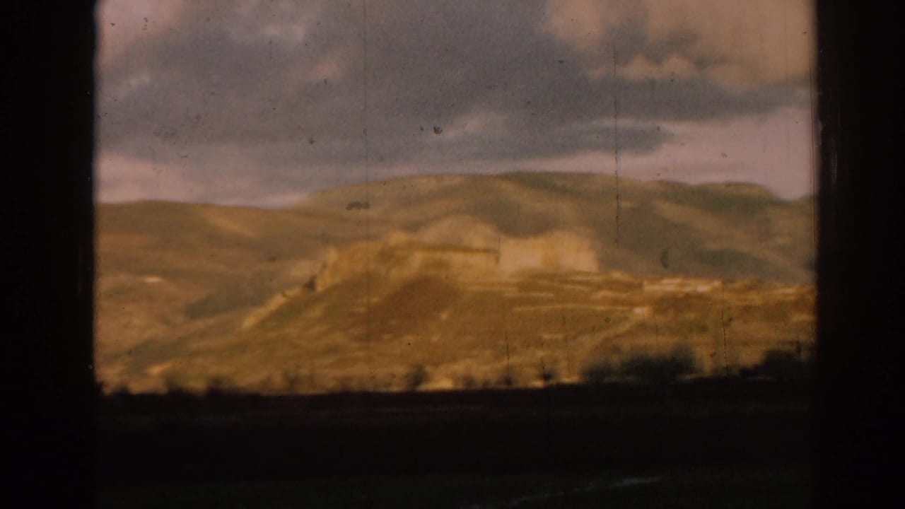 1962 Ephesus-area landscape with ancient-looking ruins and hillside buildings beneath a heavy cloudy sky.