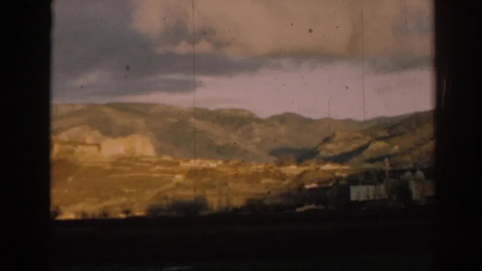Mid-century 8mm travel view of the Ephesus hillside, with distant ruins, white buildings, and layered hills under clouds.
