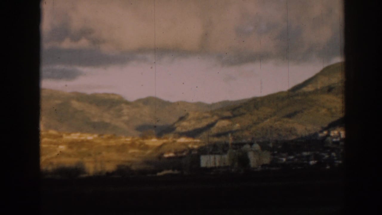 Distant village below green hills, seen through dark film-frame borders.