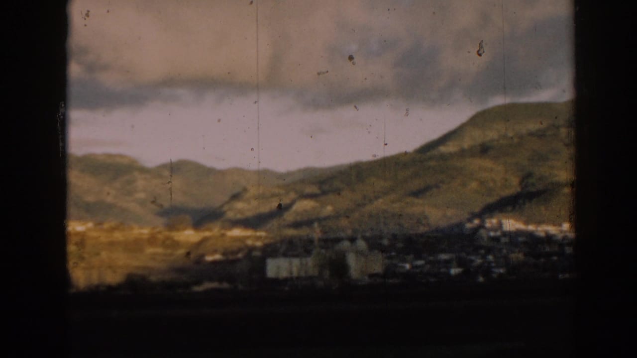 Green hills and a small valley settlement framed by dark vertical borders.
