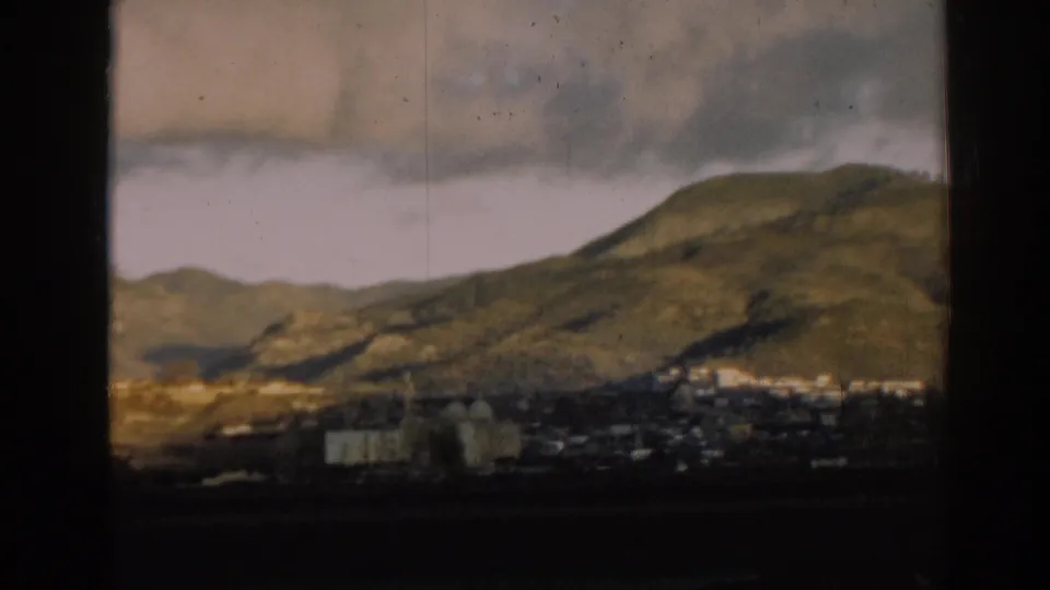 A soft 8mm frame shows hillside terrain near Ephesus with a small cluster of buildings along the lower edge.