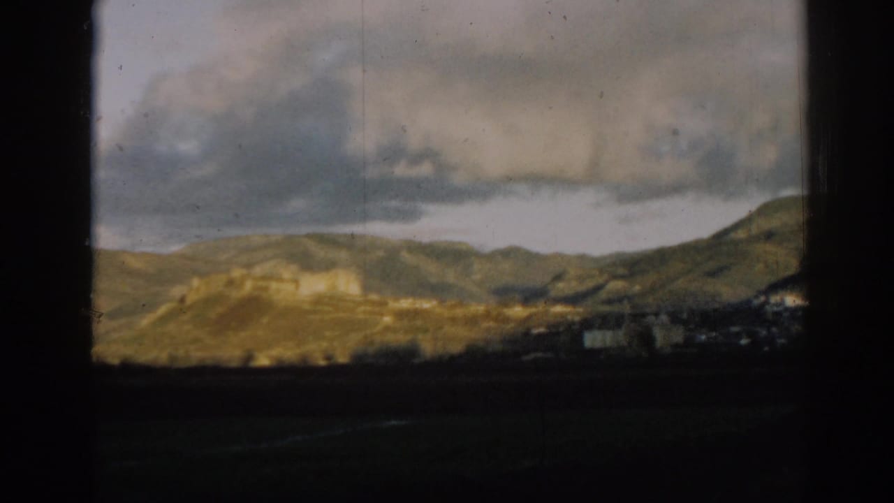 Distant hills under large clouds with a dark foreground and film-frame borders.