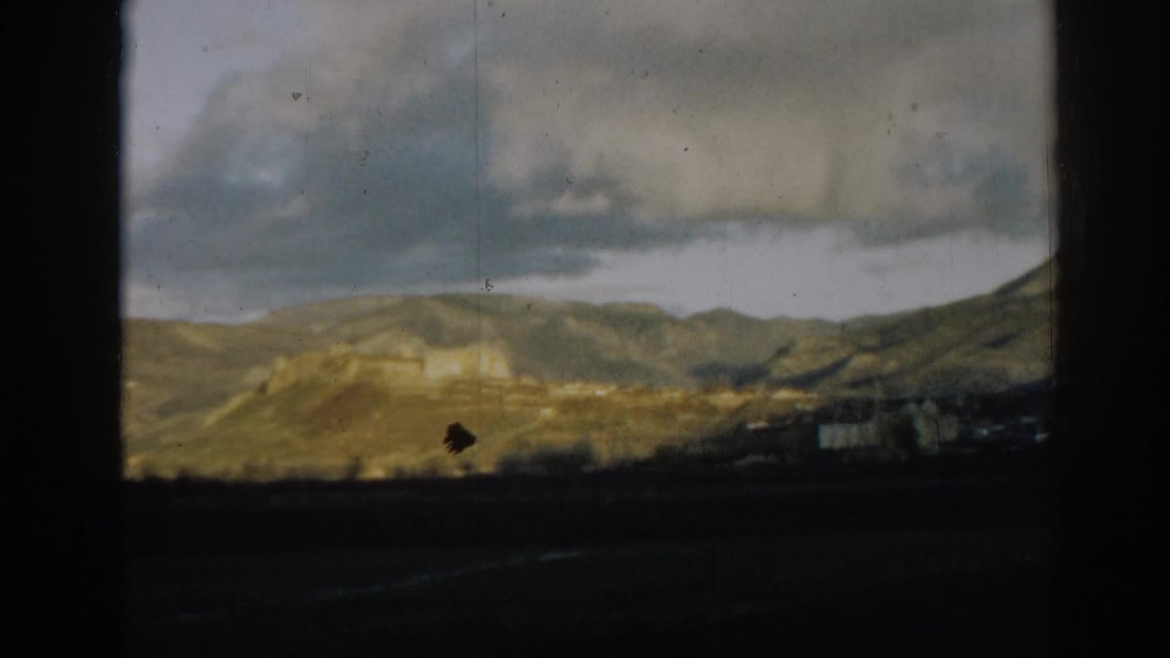 1962 8mm view near Ephesus, Turkey, with a distant hilltop structure, low settlement forms, and heavy cloud cover.