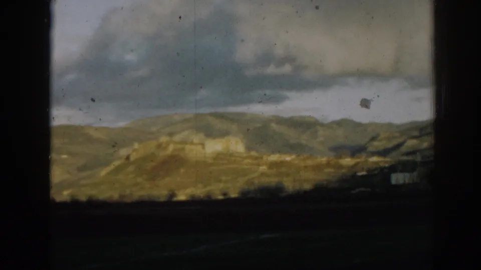 1962 8mm home-movie frame near Ephesus, Turkey, showing a mountain ridge, brooding clouds, and physical film marks.