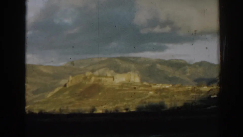 1962 8mm view near Ephesus, Turkey, with a pale structure on the hillside and layered clouds above the landscape.