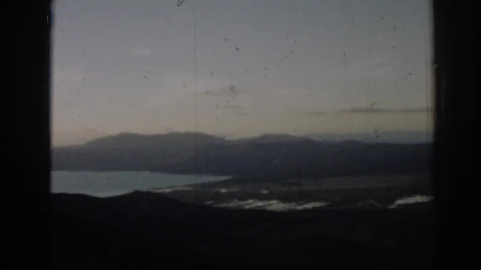 Faded 8mm frame from 1962 Turkey showing a lake below distant mountain ridges under a pale sky.