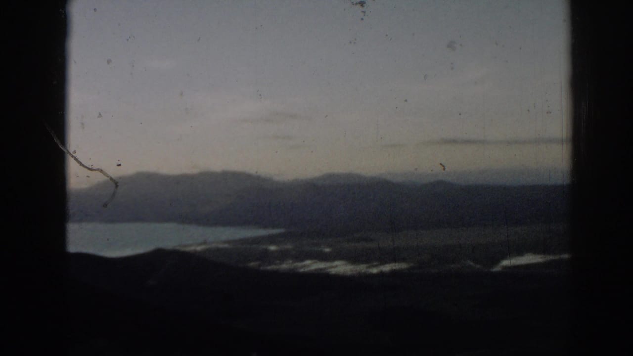 Distant mountains and water seen through a dark window-like frame.