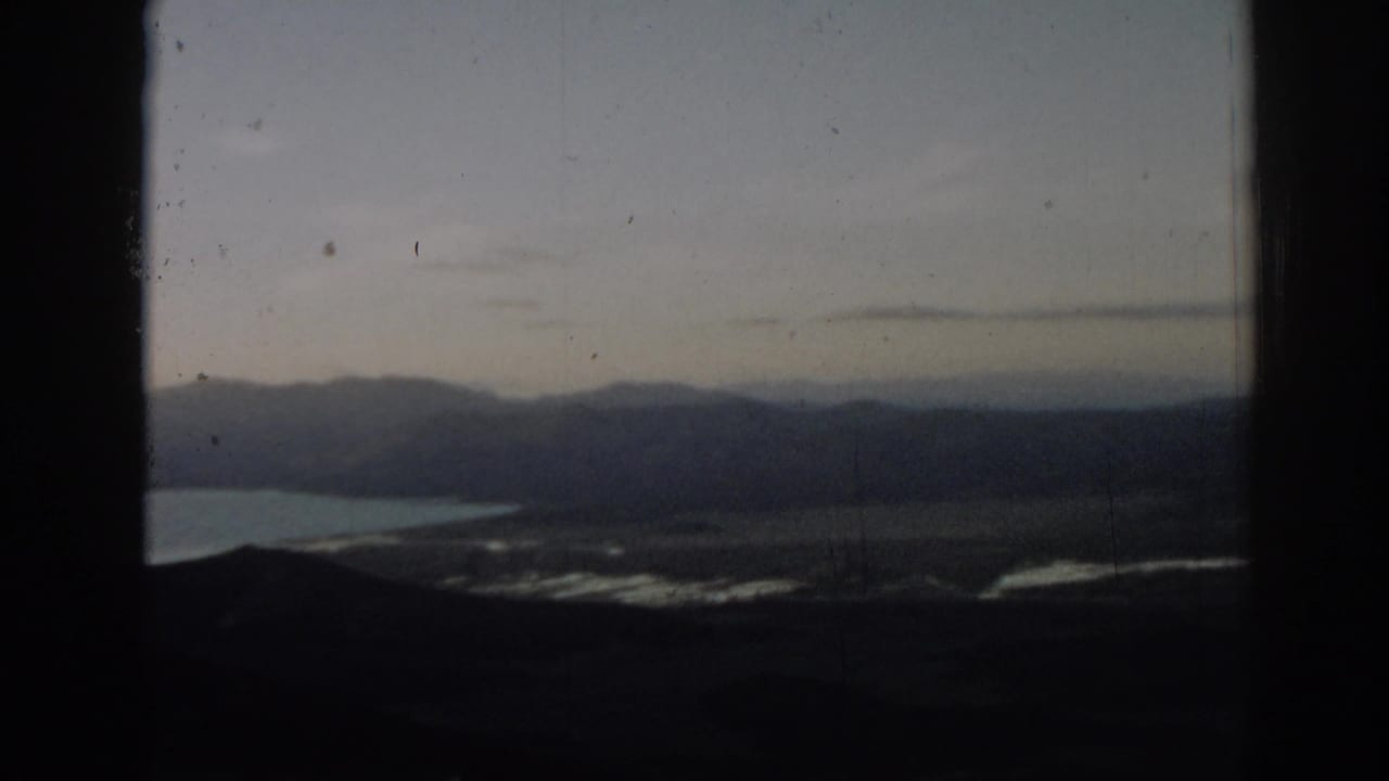 Mountain ridges and shoreline water viewed through a dark frame.