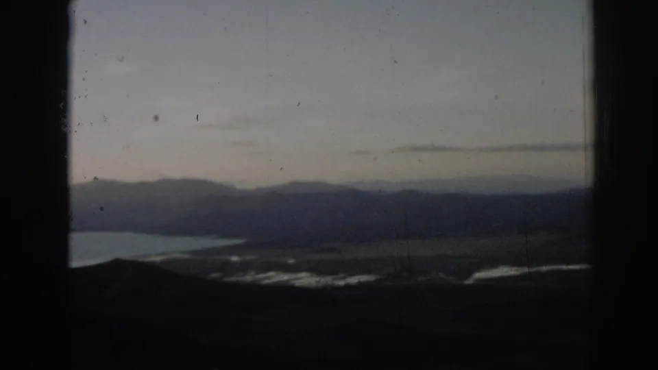 A hazy mountain range and waterline in Turkey are seen through a dark aircraft- or window-like opening.