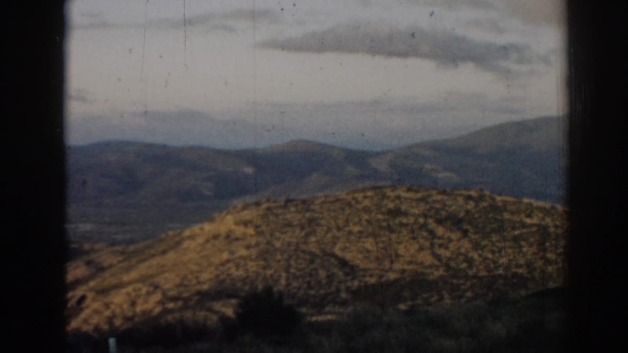 Sunlit hillside with layered mountains beyond and dark edges in the foreground.