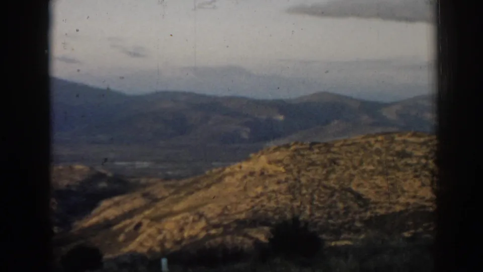 1962 home-movie landscape near Ephesus, Turkey, looking across dry hills toward hazy mountain ridges and a muted sky.