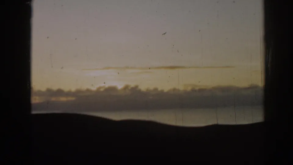 1962 8mm home-movie frame from Ephesus, Turkey, showing golden evening sky, cloud banks, water, and a dark low horizon.
