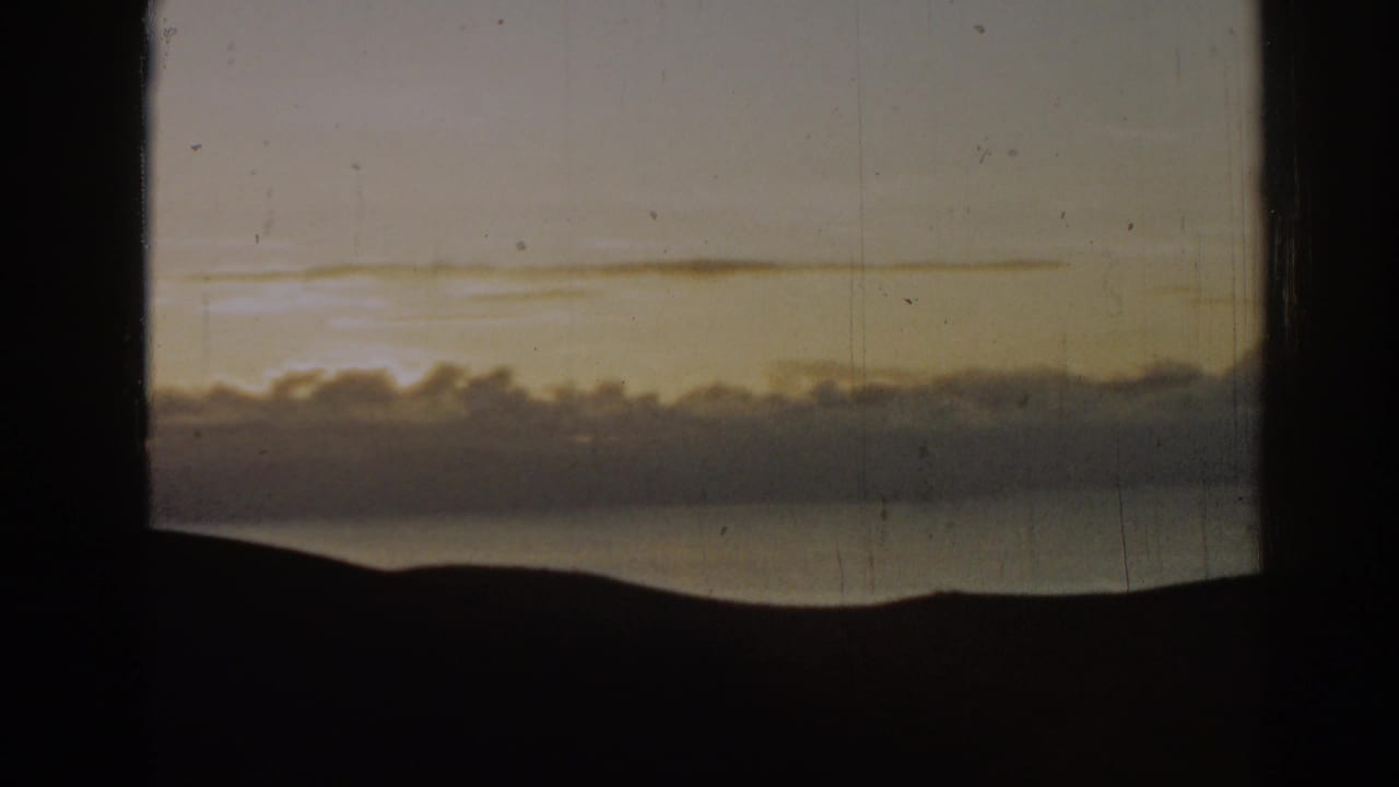 1962 Ephesus, Turkey 8mm frame with a warm sunset glow behind puffy clouds above water and a silhouetted horizon.