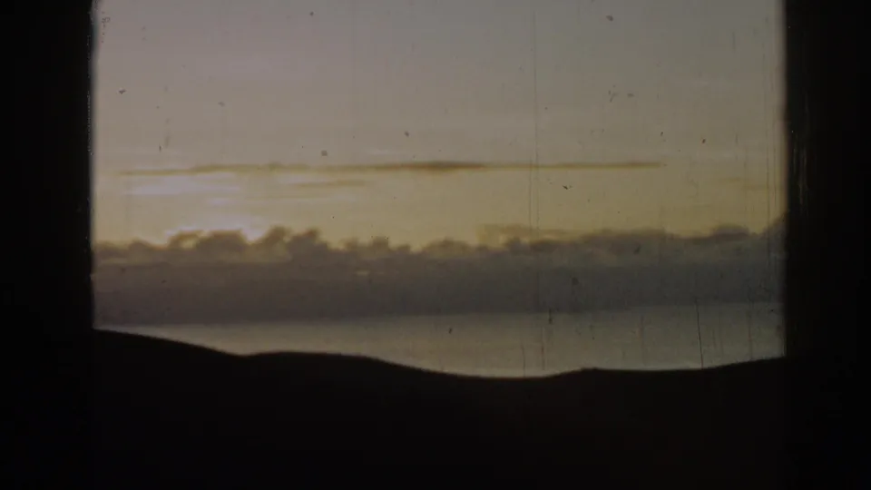 1962 Ephesus, Turkey 8mm frame with a warm sunset glow behind puffy clouds above water and a silhouetted horizon.