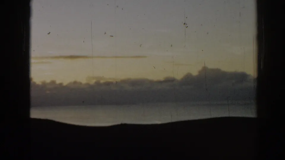1962 Ephesus, Turkey 8mm frame showing a dim sky, layered clouds, distant dark hills, and water below from a window-like viewpoint.