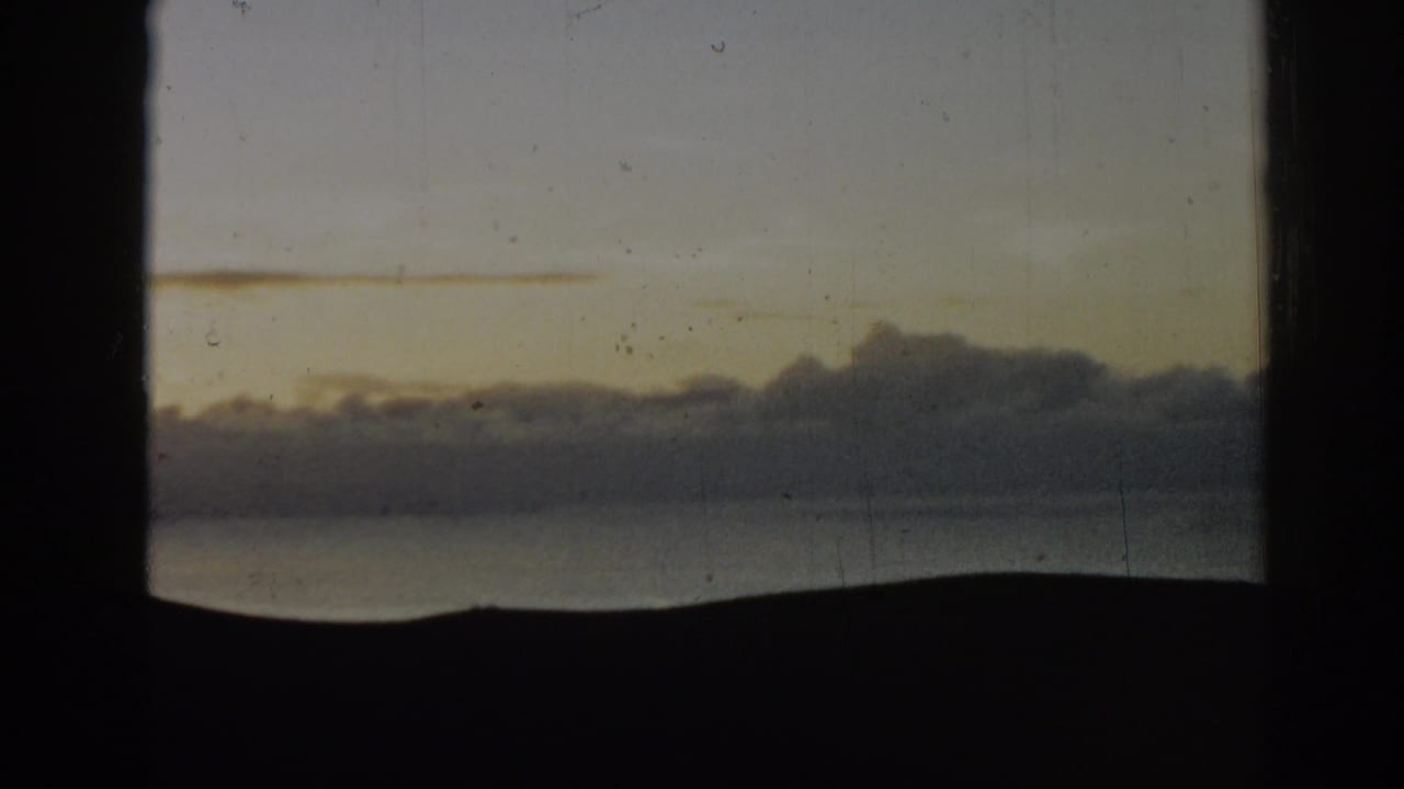 1962 Ephesus, Turkey 8mm view of a clouded sunrise or sunset sky over distant hills and water, partly obscured by the film frame edge.