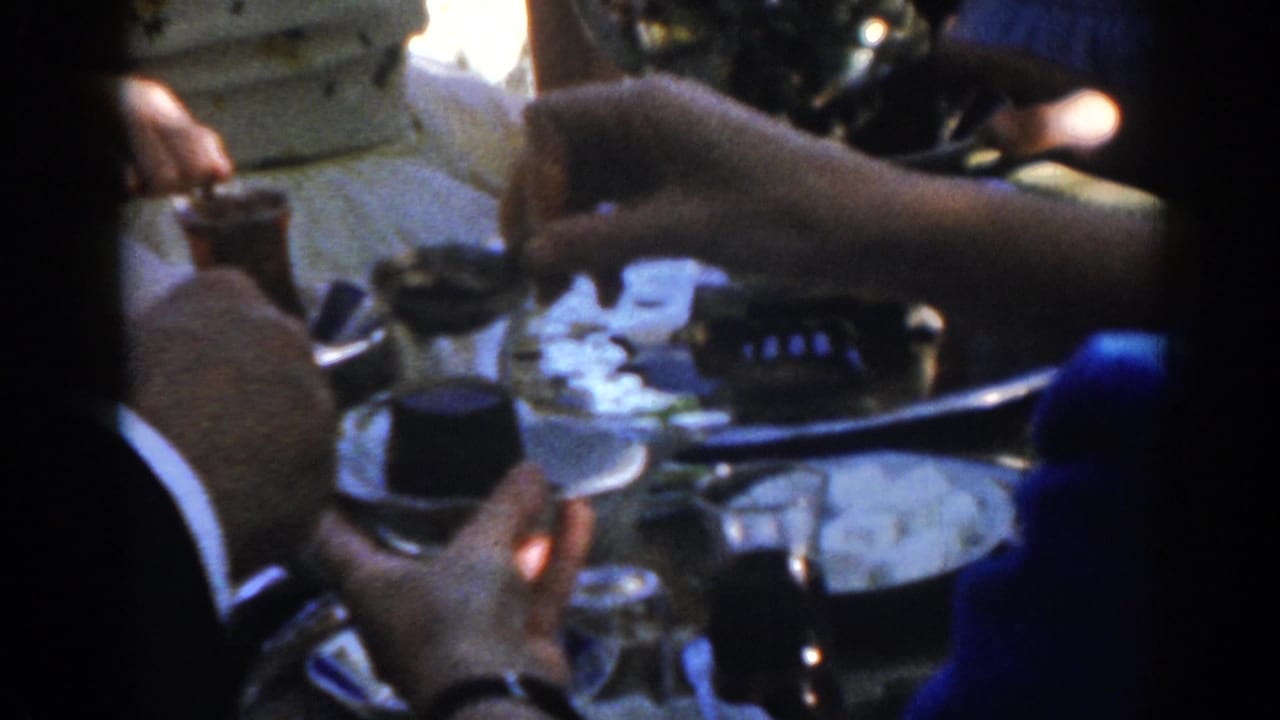 In 1962 Ephesus home-movie footage, hands gather around a metal tray while a person in a blue shirt serves a small dark drink.
