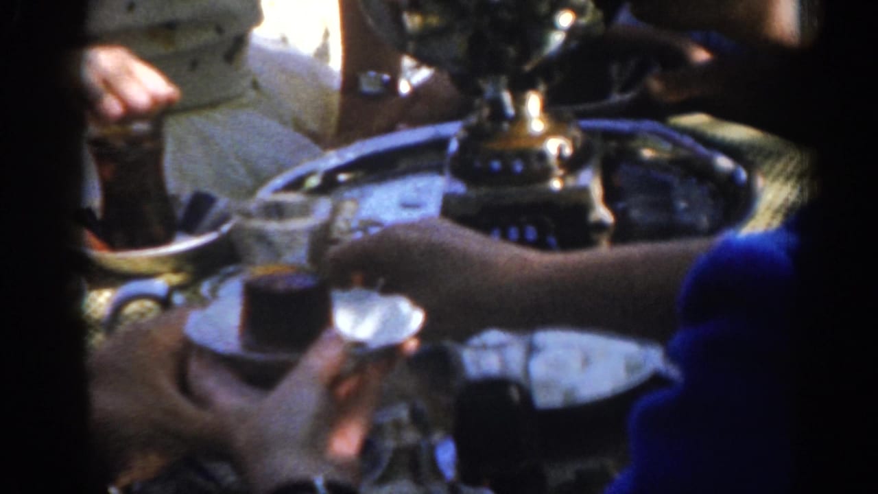 A blue-sleeved arm reaches over a tray with small glasses and a reflective pot.