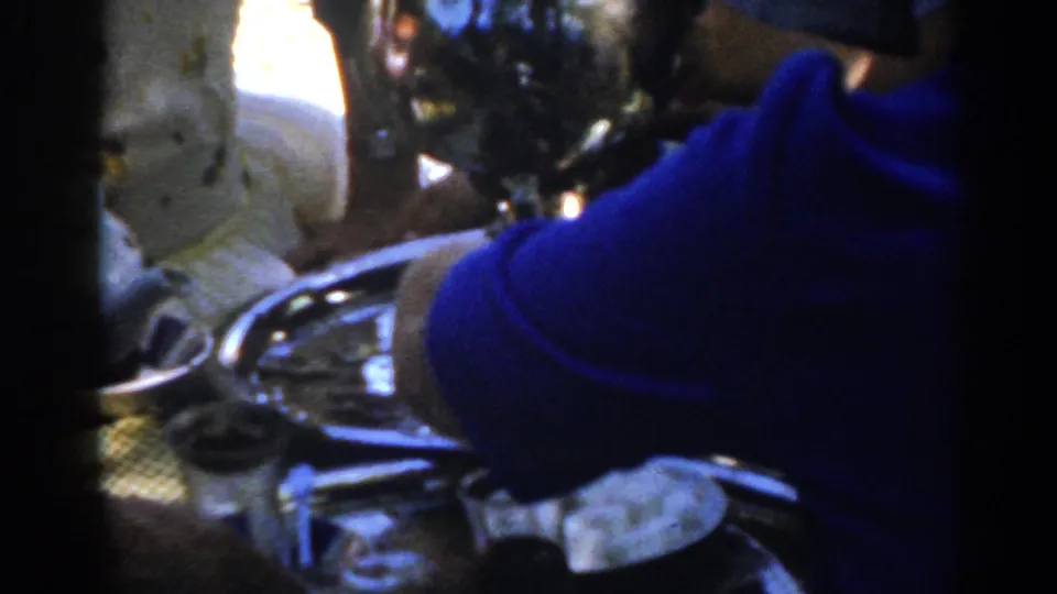 The blue-shirted figure blocks part of the close view as small glasses, a tray, and serving pieces remain visible in the Ephesus gathering.