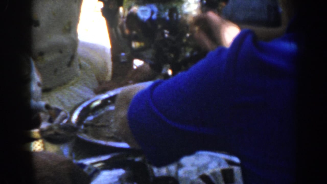 Hands operate a shiny coffee extractor above a silver tray, with a blue sweater sleeve in front.