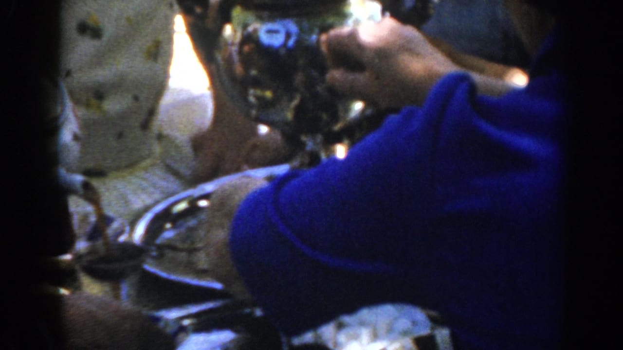 Close 8mm frame from Ephesus, Turkey, shows a hand holding a reflective coffee extractor over a tray beside a blue sleeve.