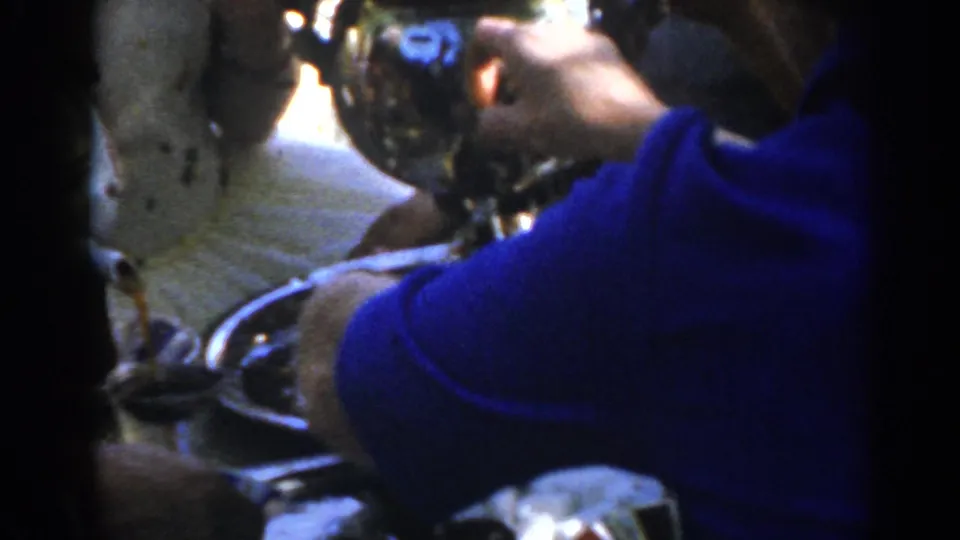 A blue-sleeved arm crosses a close view of the coffee extractor and tray in grainy 1962 Turkey home-movie footage.