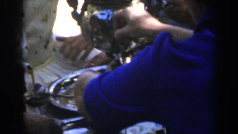 The final frame keeps the coffee extractor, tray, and blue sweater in tight handheld view, consistent with the supplied 1962 Ephesus setting.