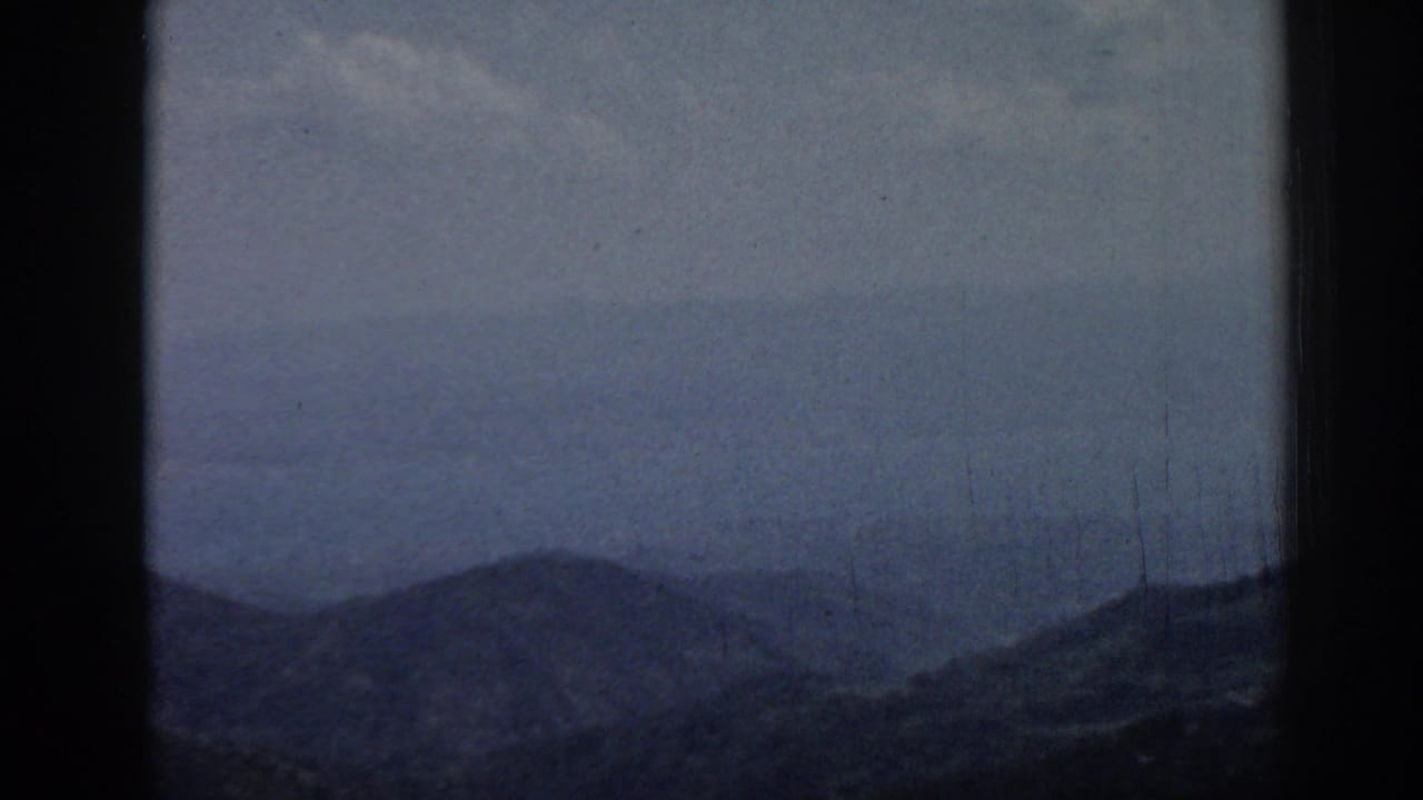 Hazy mountain ridges beneath a pale sky, framed by dark 8mm film borders.